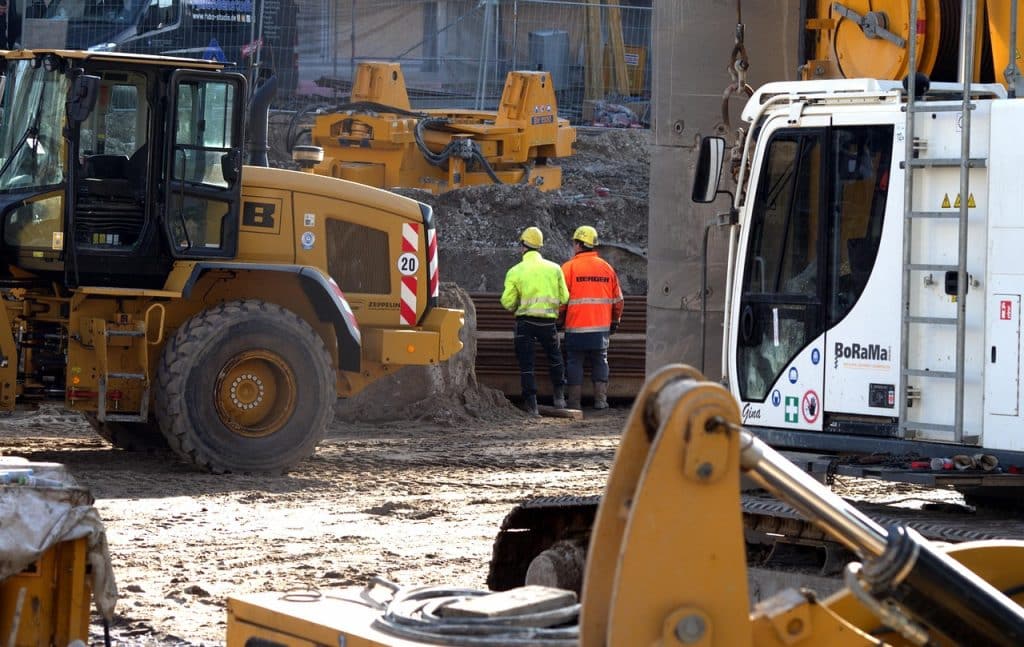 Construction site with heavy machinery and two workers in safety gear discussing project details – representing workplace accident scenarios relevant to Robert Pahlke Law Group.